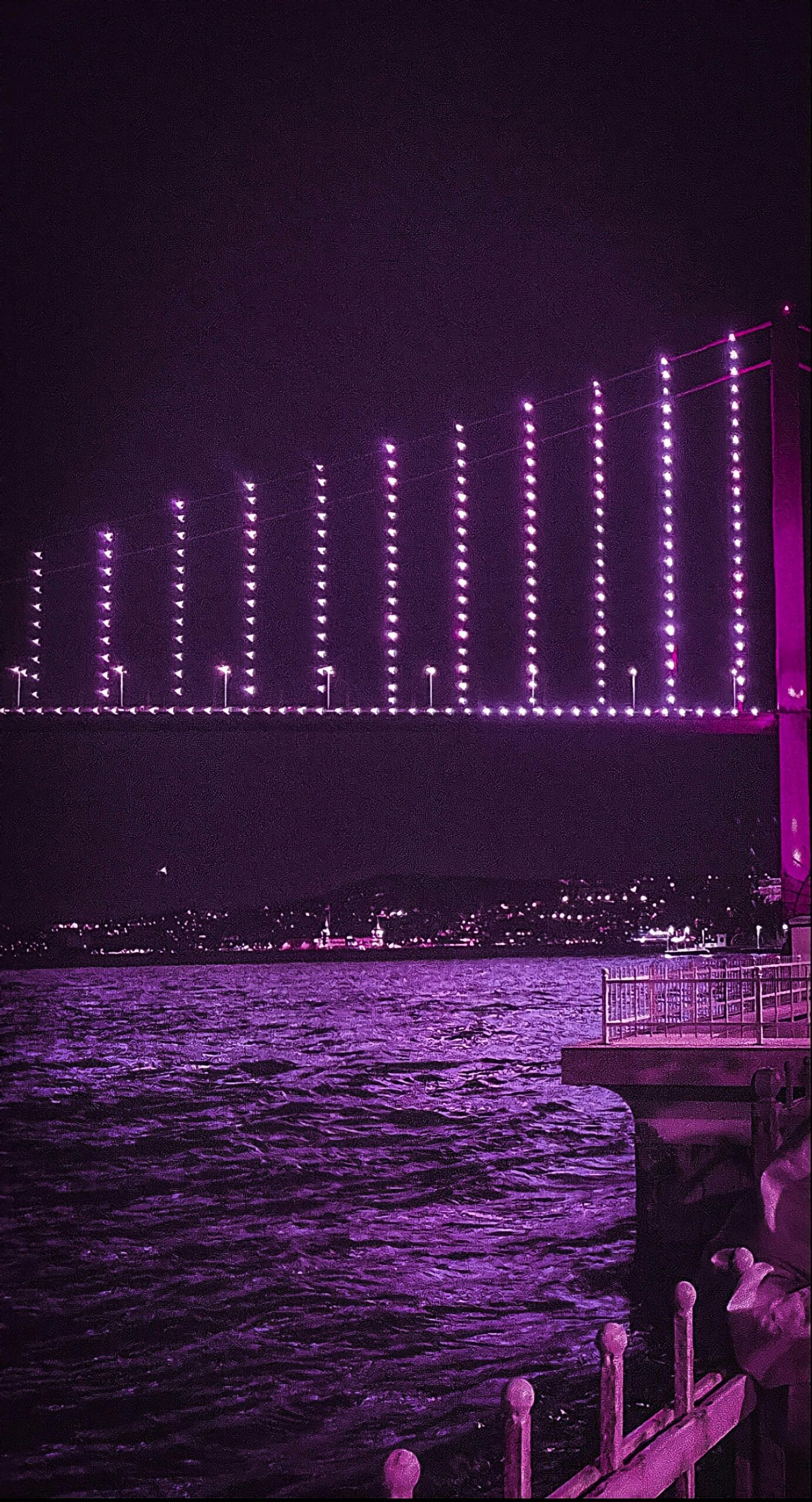 A stunning purple-lit bridge at night over a flowing river with city lights in the background.